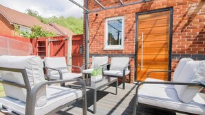 An outdoor patio with metal-framed chairs and a table, a brick wall, and a wooden door. - Hockley 4-Bed, Sleeps 13 w/ Garden & Free Parking (Birmingham)