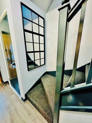 A room with a large window, a staircase, and a door leading to another area. - Hockley 4-Bed, Sleeps 13 w/ Garden & Free Parking (Birmingham)
