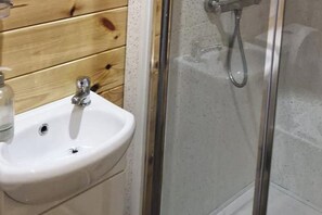 Ein Badezimmer mit einem weißen Waschbecken, einer Wand aus Holzpaneelen und einer gläsernen Dusche.