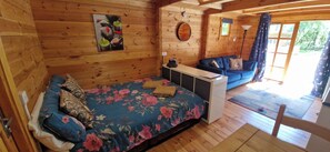 A wooden cabin interior with a bed, a sofa, and a small table.