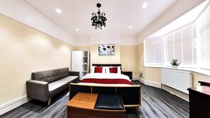 Ein Schlafzimmer mit einem Bett, einem Sofa, einer hölzernen Bank, einer Chandelüster, einer Heizung und einem Fenster mit Jalousien.