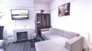 Ein Wohnzimmer mit einer Couch, einem an der Wand montierten Fernseher, einem Schrank und einem Kamin.