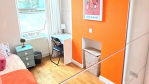 A bedroom with a bed, a desk, a chair, a window, and an orange accent wall. - Apartment Sleeps 8 in Fulham-Chelsea (London)