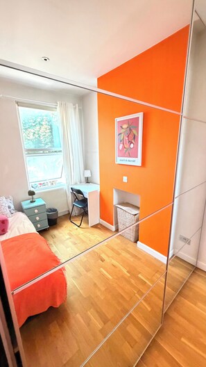 Ein Schlafzimmer mit Bett, Schreibtisch, Stuhl, Fenster und einer orangen Akzentwand.
