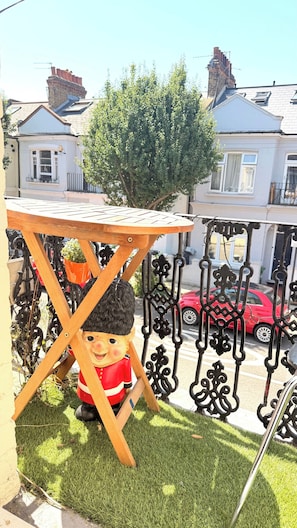Ein Balkon mit einem kleinen Tisch, einer Dekofigur und einem roten Auto im Hintergrund.