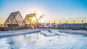 Ein Pool auf dem Dach mit Liegestühlen und einer Sonnensegel-Struktur.