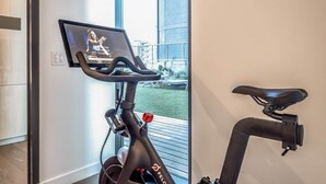 Ein stationäres Fahrrad mit einem Bildschirm, der eine trainierende Frau zeigt, einem Sitz und einer Steuerung.