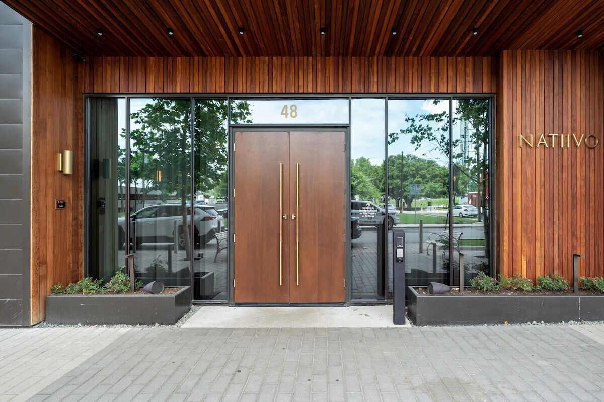 A modern building entrance with a wooden facade, a large glass door with the number 48, and a sign reading 'NATIIVO'.