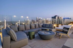 Eine Dachterrasse mit einer modernen Sofagarnitur, einem runden Couchtisch und Blick auf die Skyline der Stadt im Abendrot.