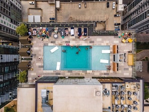 Vista aérea de uma área de piscina no terraço, com piscina, espreguiçadeiras e um estacionamento.
