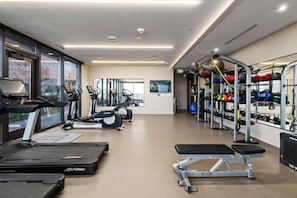 A gym with treadmills, elliptical machines, a weight bench, and a squat rack with weights. - 1906 ATX Modern Condo │ Rooftop Pool, Rainey St Views (Austin)