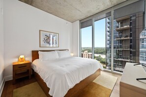 Ein modernes Hotelzimmer mit einem großen Bett, einem Schreibtisch und Blick auf die Stadt durch große Fenster.