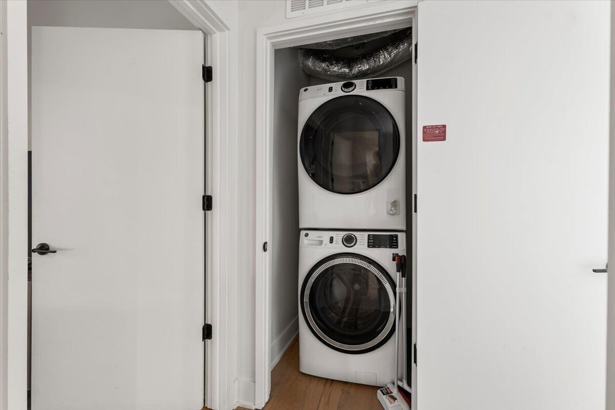 A laundry room with stacked washers and dryers, a white door, and a red safety sign.