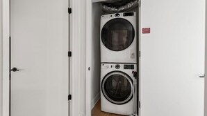 A laundry room with stacked washers and dryers, a white door, and a red safety sign. - Lake View Penthouse | Luxury On Rainey *Sleeps 8* (Austin)