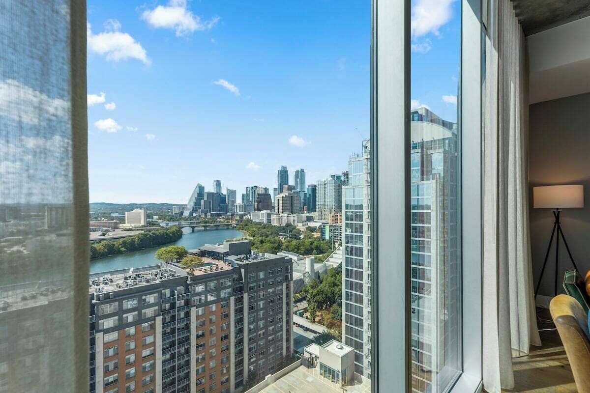A high-rise building with a view of a city skyline, a river, and a modern interior with a lamp and a chair.