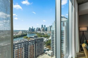 A high-rise building with a view of a city skyline, a river, and a modern interior with a lamp and a chair.