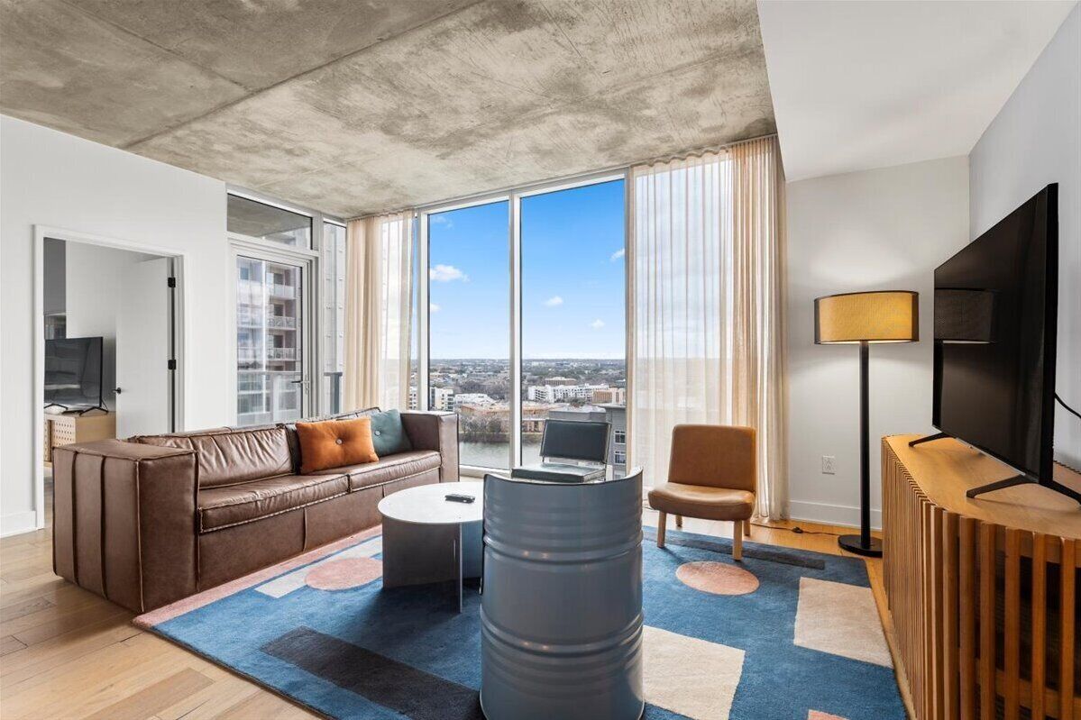 A modern living room with a sofa, coffee table, and a large window offering a city view.