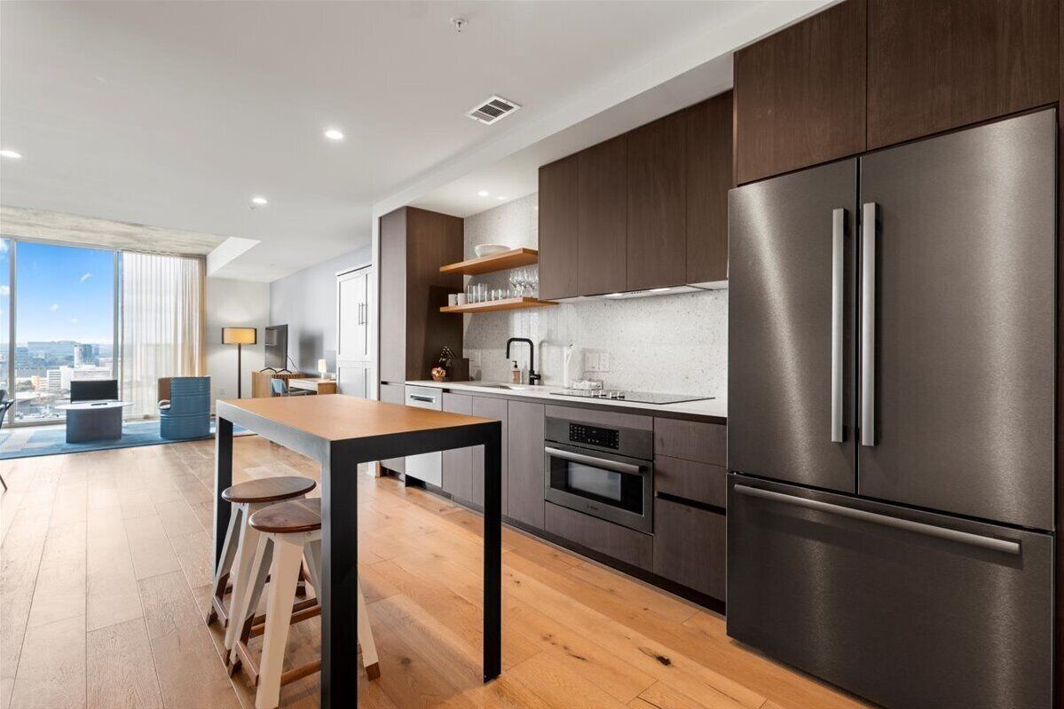 A modern kitchen with dark wood cabinets, stainless steel appliances, and a large window overlooking a cityscape.