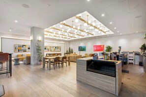 A modern hotel lobby with a dining area, a reception desk, and a large open space with ceiling lights. - 2601 ATX Skyline Corner Retreat | Rooftop Pool, Skyline Views, Rainey St (Austin)