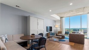 Uma sala de estar moderna com sofá, mesa de jantar, cadeiras, televisão e uma grande janela com vista para a cidade.