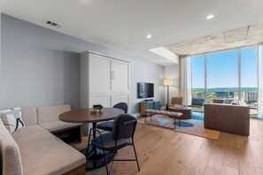 Ein modernes Wohnzimmer mit einer Couch, einem Esstisch, Stühlen, einem Fernseher und einem großen Fenster mit Blick auf die Stadt.
