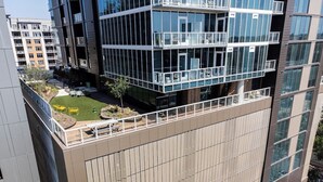 A modern building with a flat roof terrace, a courtyard with seating, and a large glass facade. - Sunset Condo | Downtown Austin *Rooftop Pool* & City Views! (Austin)