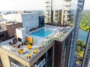 Una piscina en la azotea con barandillas de cristal, mobiliario exterior y vistas a un río y edificios circundantes.