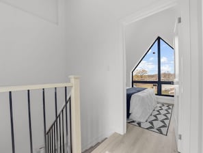 Eine schmale Treppe führt zu einem Schlafzimmer mit einem Bett, einem Fenster und einem Teppich mit geometrischem Muster.