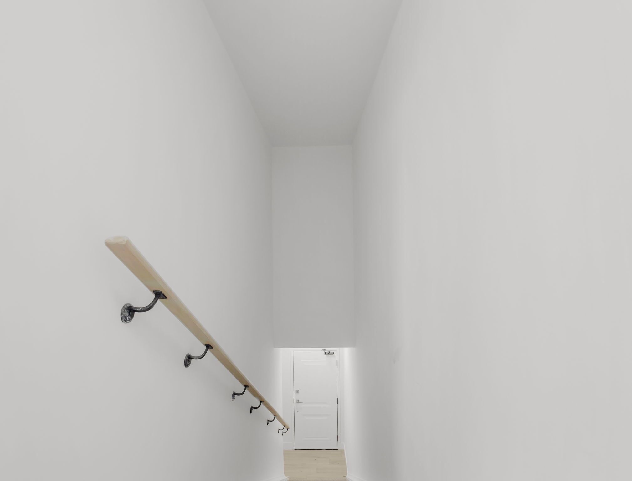 Un escalier étroit aux murs blancs, doté d’une rampe en bois et d’écrochets en métal.