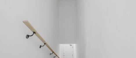 Un escalier étroit aux murs blancs, doté d’une rampe en bois et d’écrochets en métal.