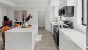 Uma cozinha moderna com armários brancos, eletrodomésticos de aço inoxidável e uma ilha central com um vaso de plantas secas.