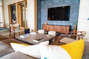 Ein modernes Wohnzimmer mit einem großen Flachbildfernseher, einer Holzkassette und einer gemütlichen Sitzecke mit Kissen.