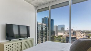A bedroom with a large bed, a flat-screen TV on a cabinet, and a city view through large windows. - Sunny Corner DT Suite * Pool * Walk to 6th, Rainey (Austin)