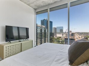 Ein Schlafzimmer mit einem großen Bett, einem Flachbildfernseher auf einer Kommode und Stadtblick durch große Fenster.