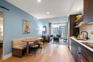 A modern kitchen with a built-in oven, a dining area with a wooden table and chairs, and a large window offering a view of the city. - 1211 ATX Longhorn Chic │ Hill Country Style, Rooftop Pool (Austin)