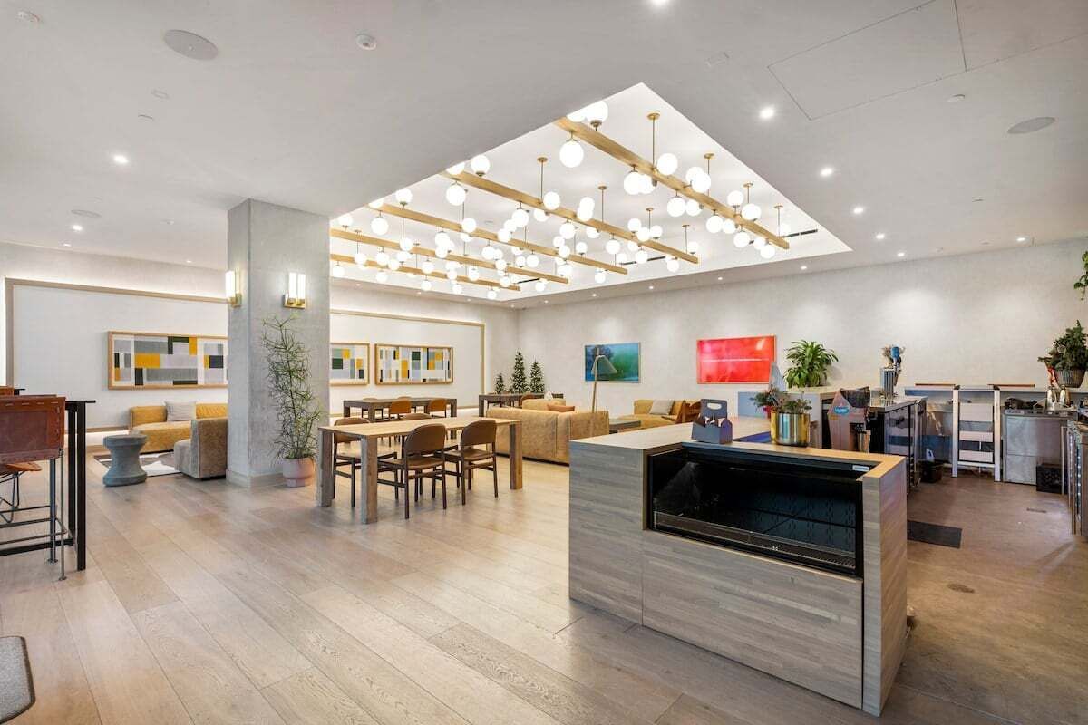 A modern hotel lobby with a dining area, a fireplace, and a ceiling with hanging lights.