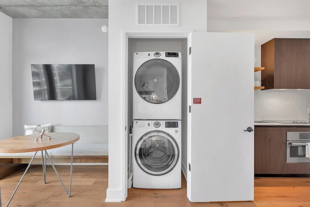 A compact kitchen with a built-in oven, a washing machine, and a dining area with a round table.