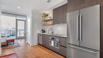 A modern kitchen with a large refrigerator, oven, and sink. There is a balcony with a view of the city.