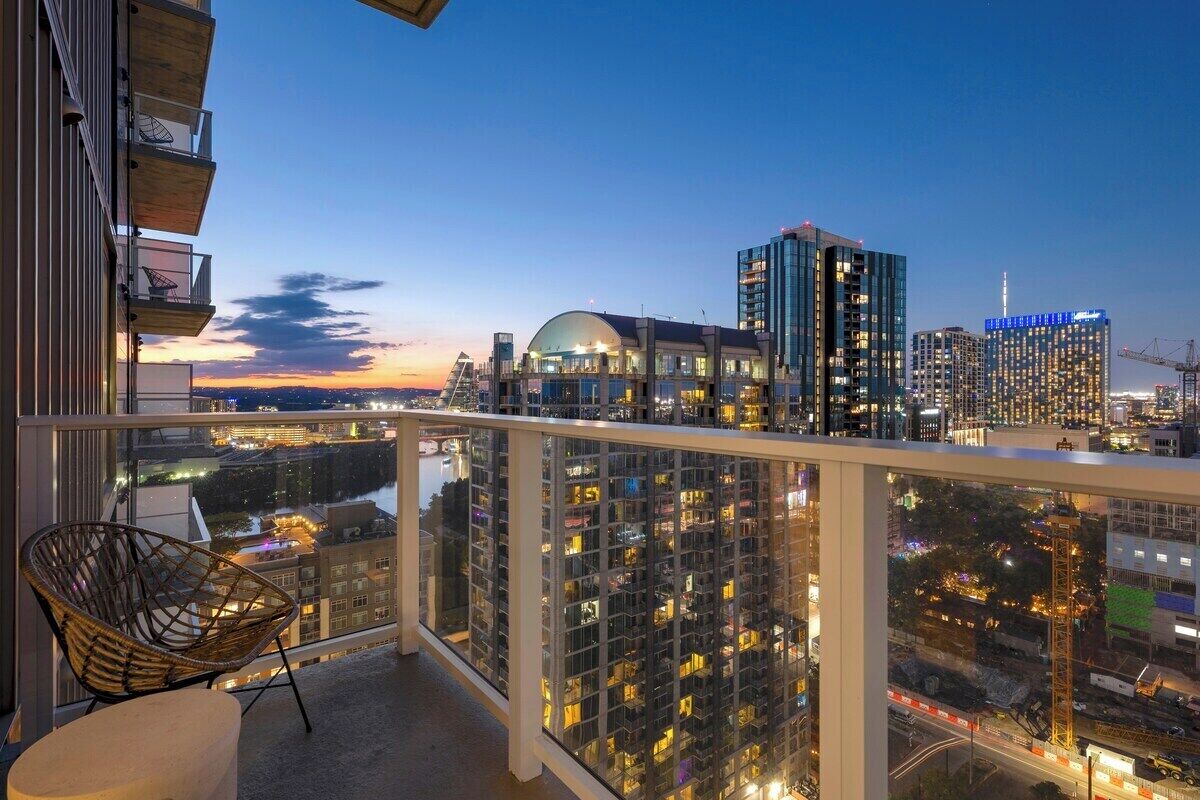 A balcony with a view of a cityscape at dusk, including high-rise buildings and a body of water.