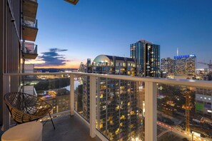 A balcony with a view of a cityscape at dusk, including high-rise buildings and a body of water. - Unique Artistic Corner Downtown Sky Condo | On Rainey St. + Rooftop Pool! (Austin)