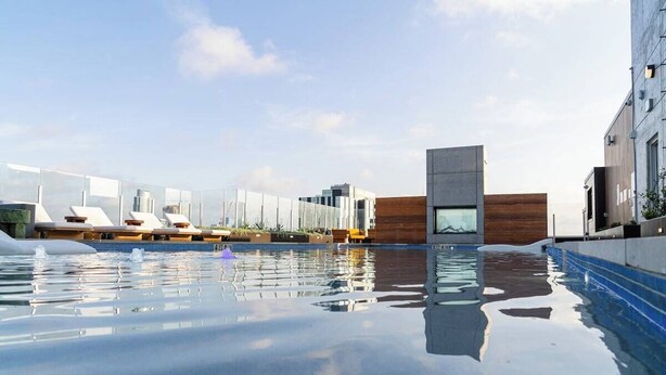 A modern pool area with a clear sky, a wooden deck, and a glass building in the background. - Rainey Street Lux High Rise Condo | Rooftop Pool! (Austin)