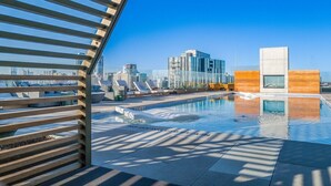 A rooftop pool with lounge chairs, a modern building in the background, and a clear blue sky. - Austin Lux Suite | Downtown Views + Prime Location! (Austin)