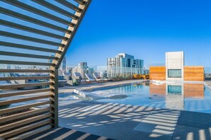 A rooftop pool with lounge chairs, a modern building in the background, and a clear blue sky. - Austin Lux Suite | Downtown Views + Prime Location! (Austin)