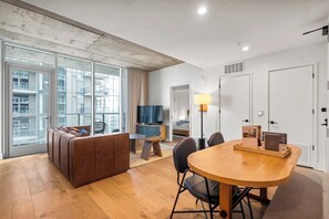 Ein modernes Hotelzimmer mit großem Fenster, einer Couch, einem Esstisch und einem Fernseher.