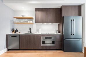 Eine moderne Küche mit dunklen Holzschränken, einem Edelstahlkühlschrank, einem Backofen von Bosch und einer Arbeitsplatte mit Spüle und Geschirr.