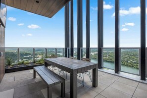 A balcony with a view of a river and greenery, a wooden table, and chairs. - 1909 ATX Lux Suite | Downtown Rainey St Luxury, Rooftop Pool & Skyline Views (Austin)