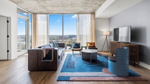 A modern living room with a large window, a sofa, a coffee table, and a TV. - Riverside Penthouse in heart of Rainey - Sleeps 6 (Austin)