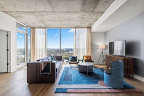 Ein modernes Wohnzimmer mit großem Fenster, einer Couch, einem Couchtisch und einem Fernseher.