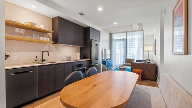 Una cocina moderna con armarios oscuros, una mesa de comedor de madera y vistas a un paisaje urbano a través de amplios ventanales.