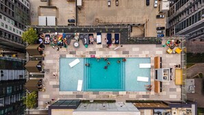 Vista aérea de una zona de piscina en la azotea, con piscina, sillas de descanso y un estacionamiento.